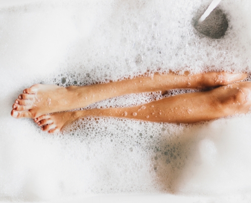 woman in a tub, with legs covered in bubbles self care