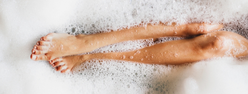 woman in a tub, with legs covered in bubbles self care