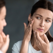 woman checking her enlarged pores in front of a mirror