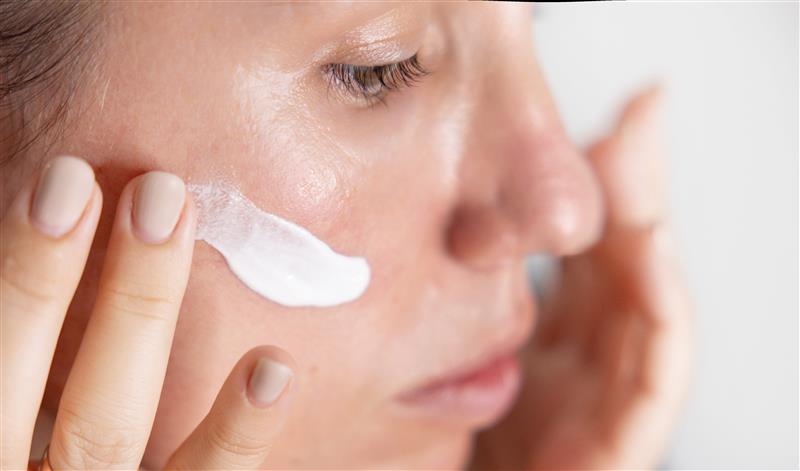 a woman applying cream on the contour of her right cheek