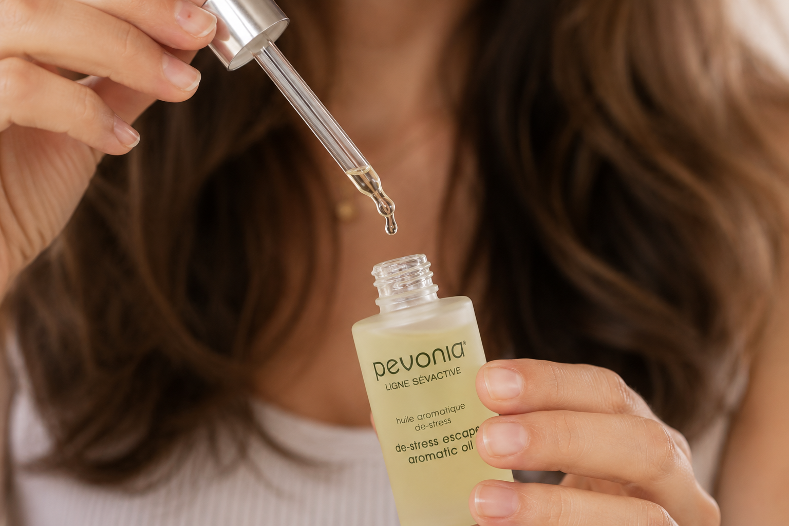 A woman's hands holding an opened bottle of Pevonia De-stress Escape Aromatic Oil
