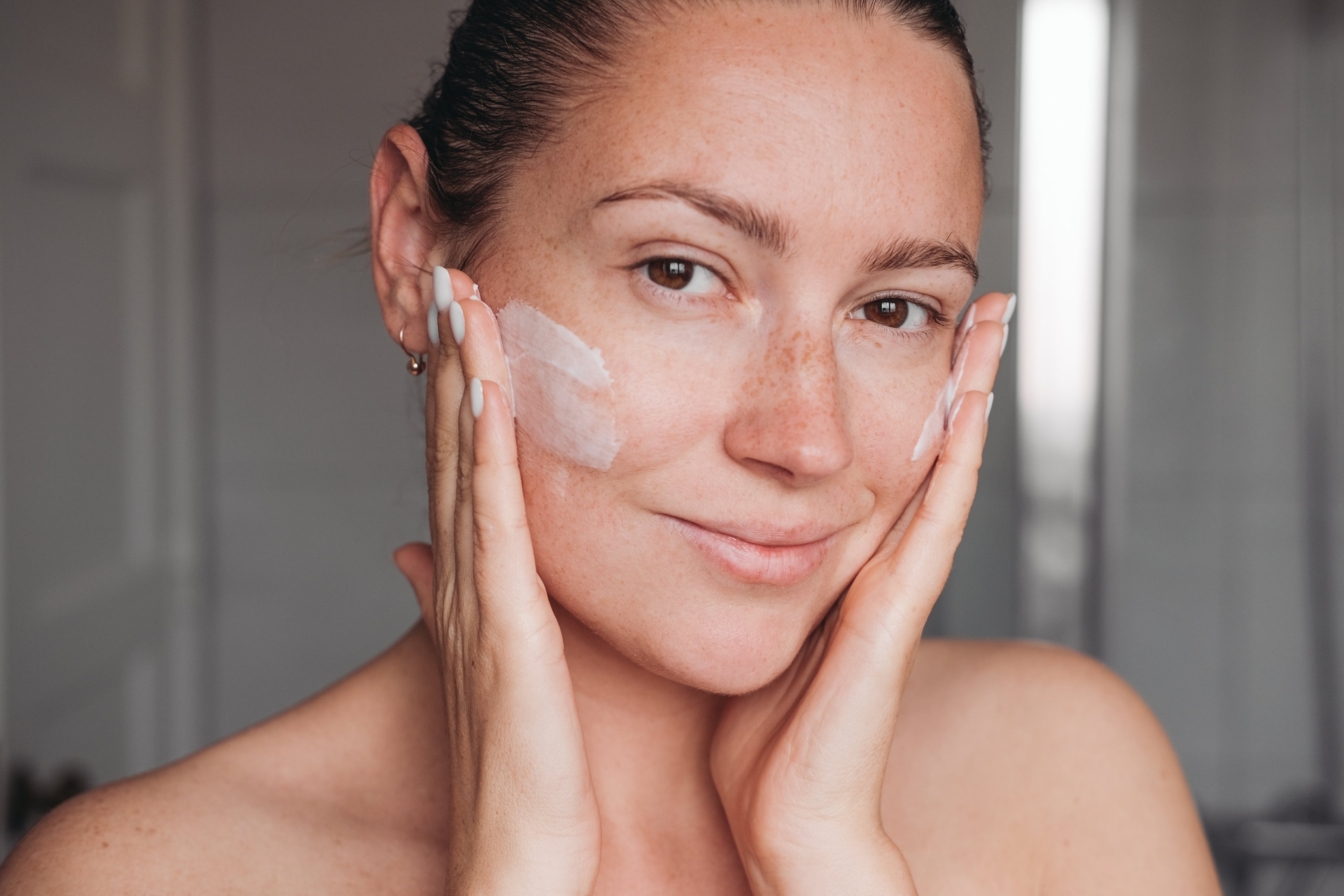 woman applying cream to both her cheeks