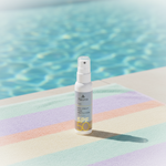 Spray bottle labeled 'NATURYS Sun Cream High Protection SPF 30 (spray) 100ml' on a striped towel by a pool