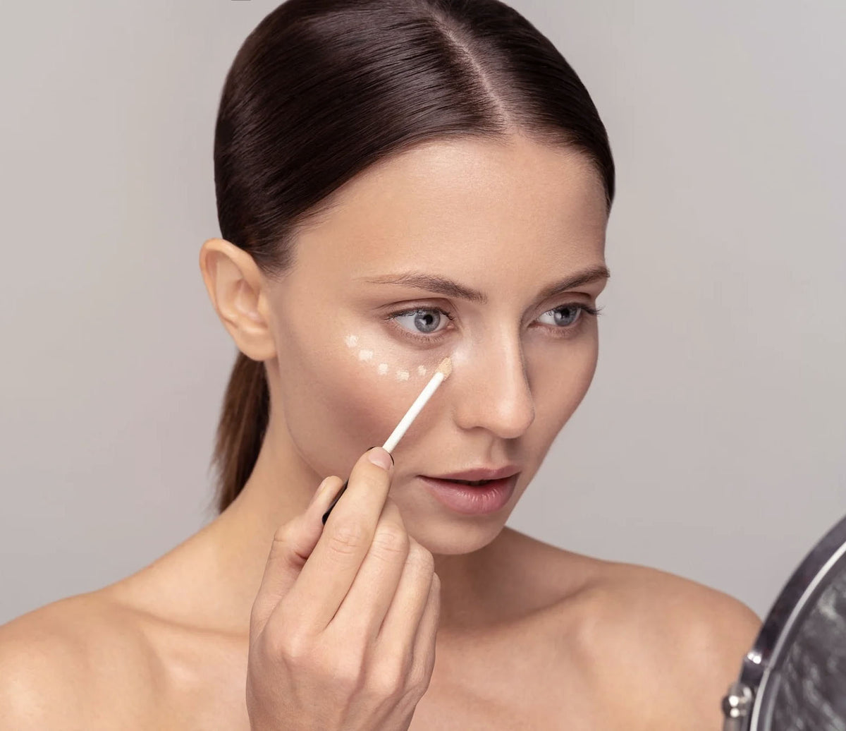 Woman applying ELES Adjustable Coverage Concealer with a cotton pad on a neutral background