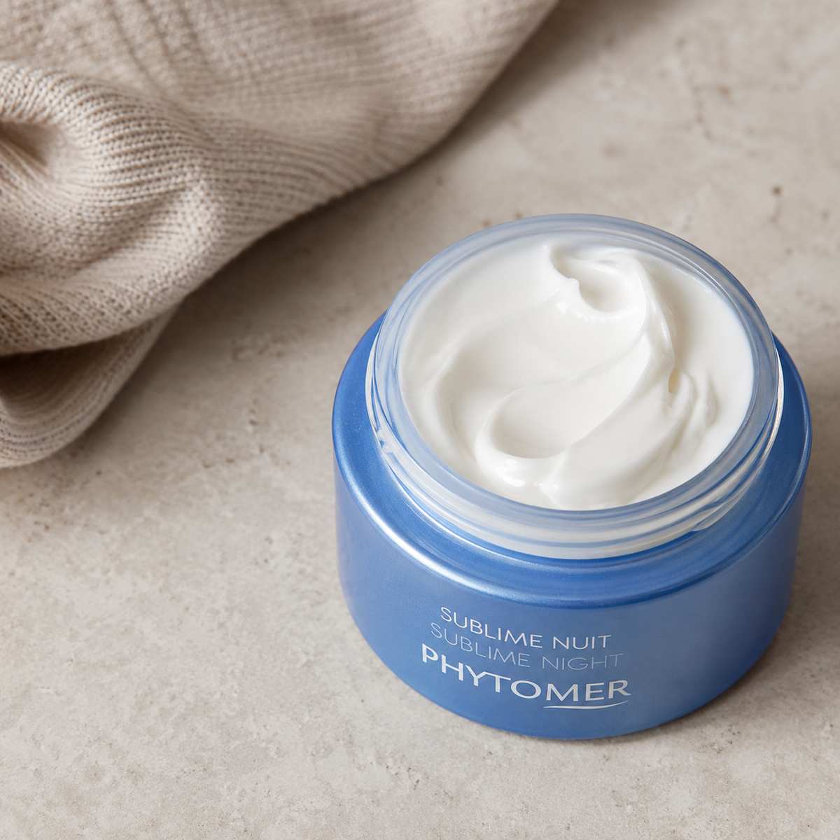 Blue jar of Phytomer Sublime Nuit cream on a beige surface