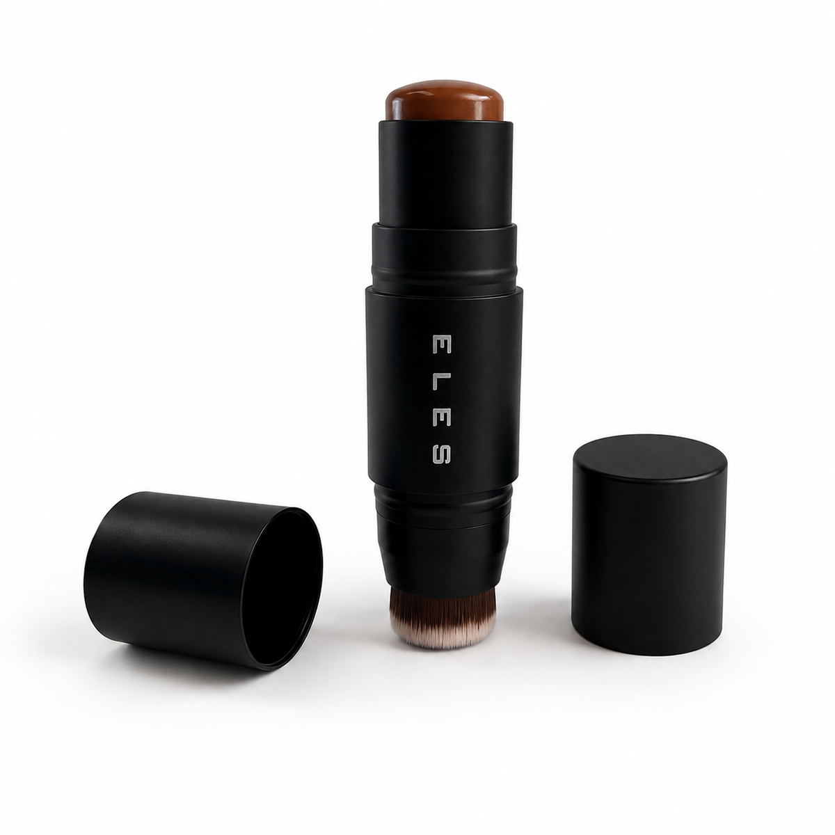 An ELES makeup stick with a black cylindrical body, shown open with the brush exposed and a brown cosmetic product visible at the top. A second black cap lies on the left, and another closed cap stands on the right, all on a clean white background.