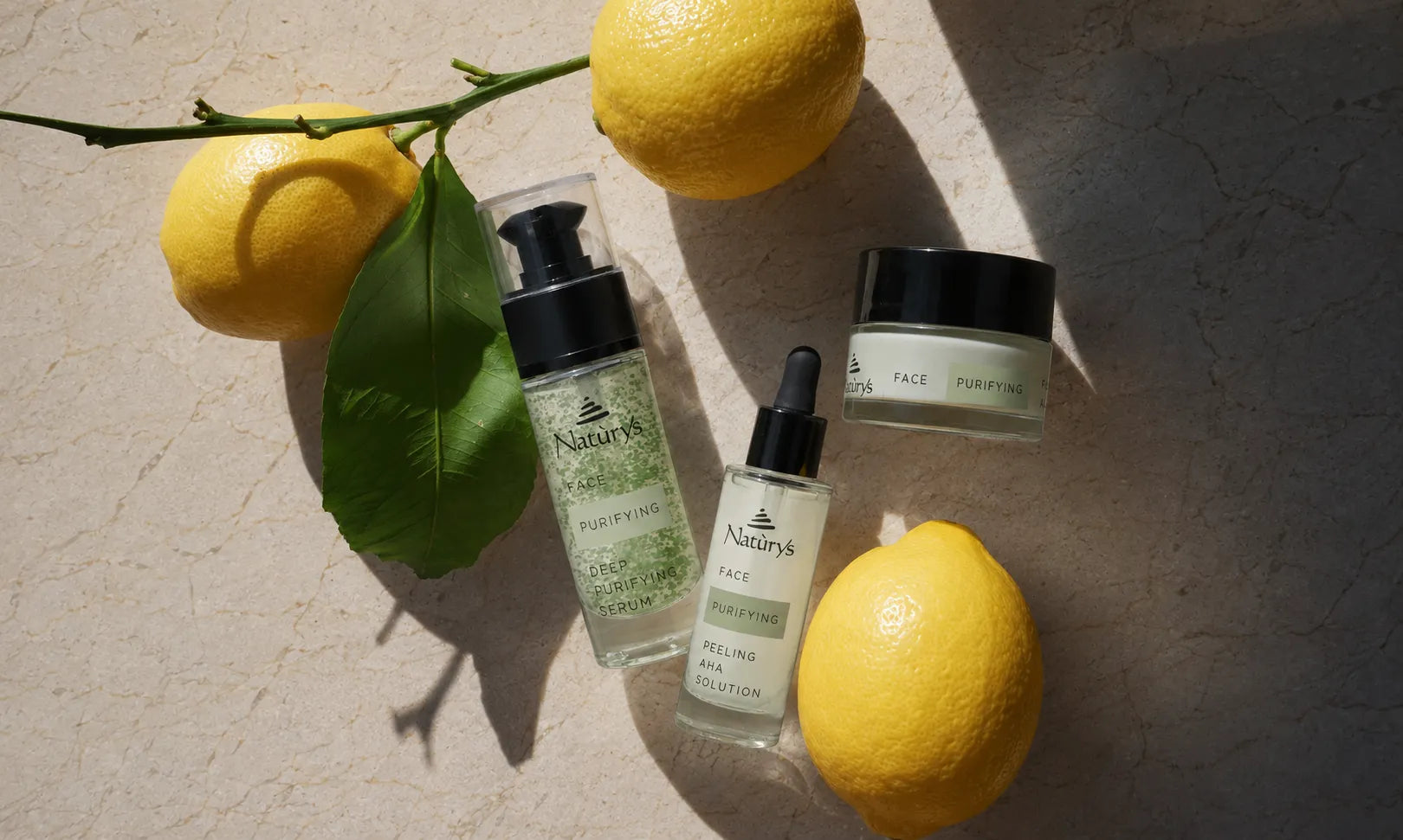 Four skincare products from Nature's Apothecary are arranged on a textured beige surface with bright yellow lemons and a green leaf. The products include a face purifying gel, a face serum, a face toner, and a face moisturizer, styled in a sunny, artistic flat-lay composition.