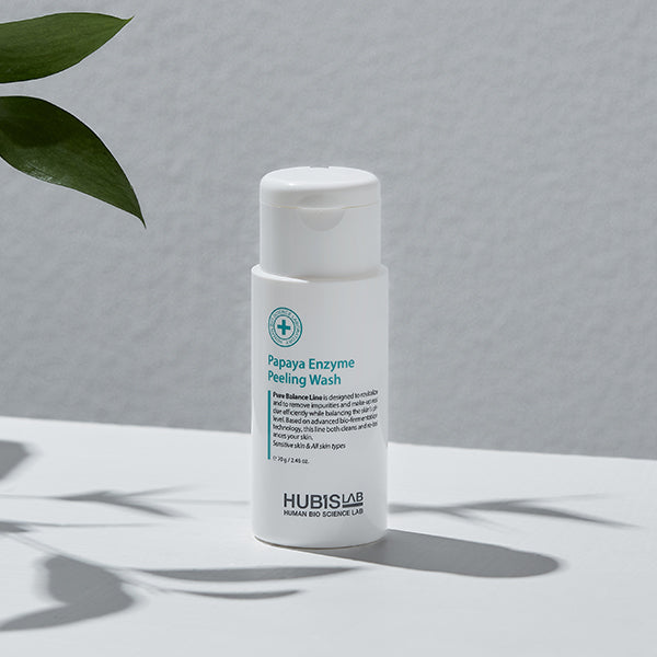 Hubislab Papaya Enzyme Peeling Wash bottle on a gray background with green leaves.