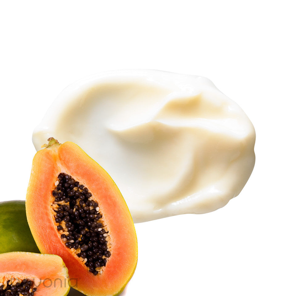 Close-up of a halved papaya with a dollop of Pevonia De-Aging Body Balm Papaya Pineapple white cream on a white background visualizing the texture of product