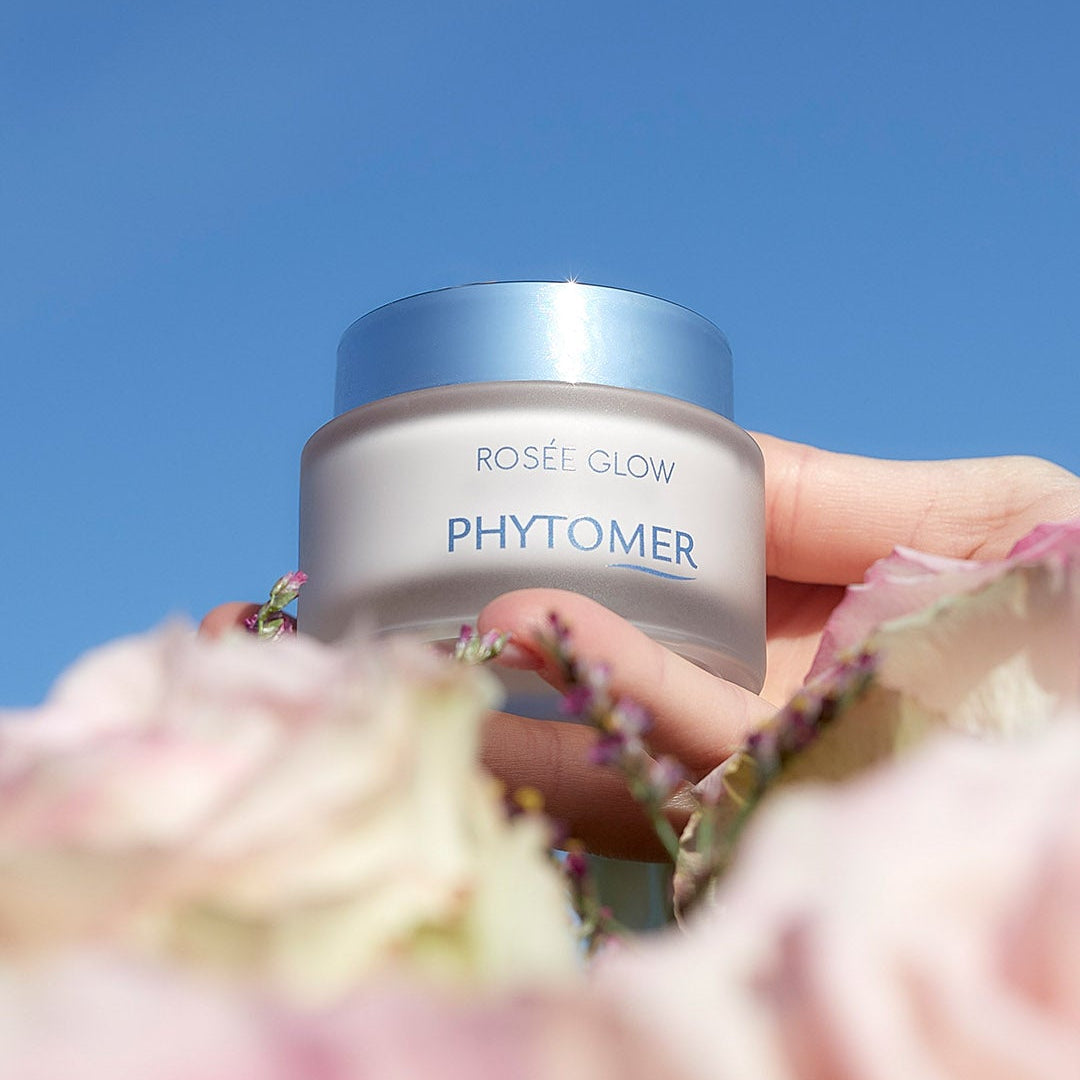 Phytomer Rosee Glow - Vitamin Radiance Plumping Cream against a blue sky with flowers in the foreground