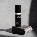 Skincare serum bottle labeled 'Vie' on a stone surface with a gray background