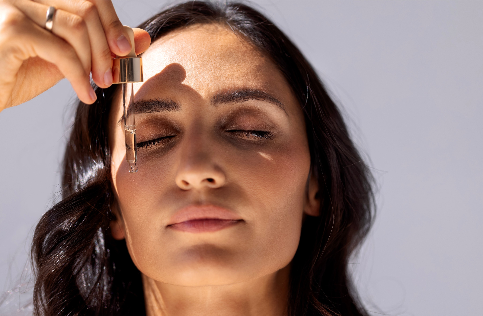 Woman applying a serum to her face against a neutral background