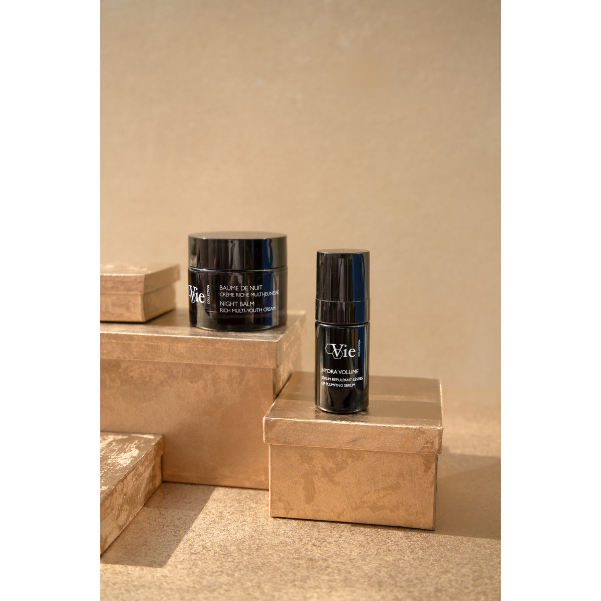 NIGHT BALM cream and Hydra Volume Lip Plumping Serum displayed on gold gift boxes