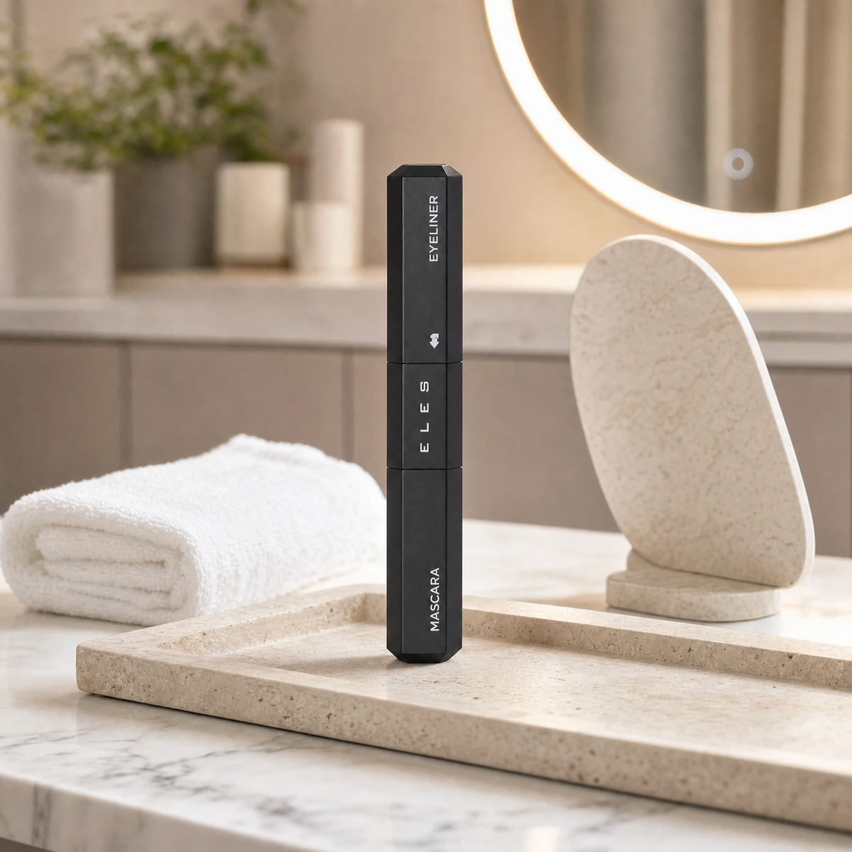 Eles 2 in 1 Mascara Liner Black  standing upright on a marble tray in a bathroom setting, with a folded white towel, a stone stand, and a softly lit mirror in the background.