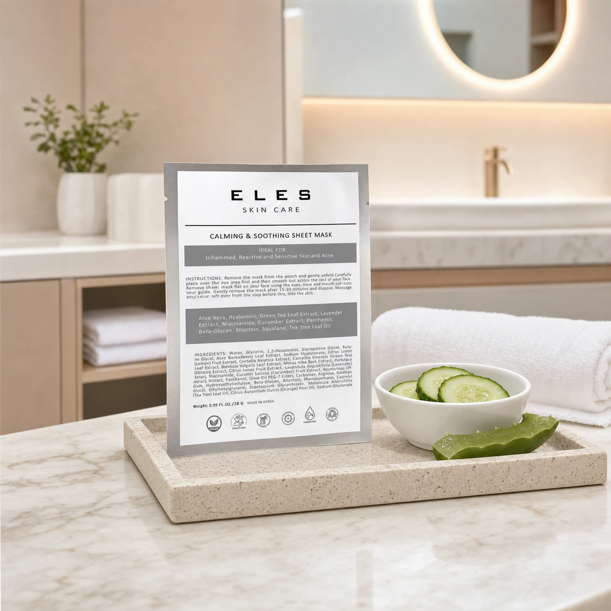 ELES Calming and Soothing Sheet Mask grey foil sachet leaning against a stone tray with cucumber slices and aloe vera on a marble clinic bench inside a premium skin clinic treatment room, ideal for professional calming facial treatment preparation