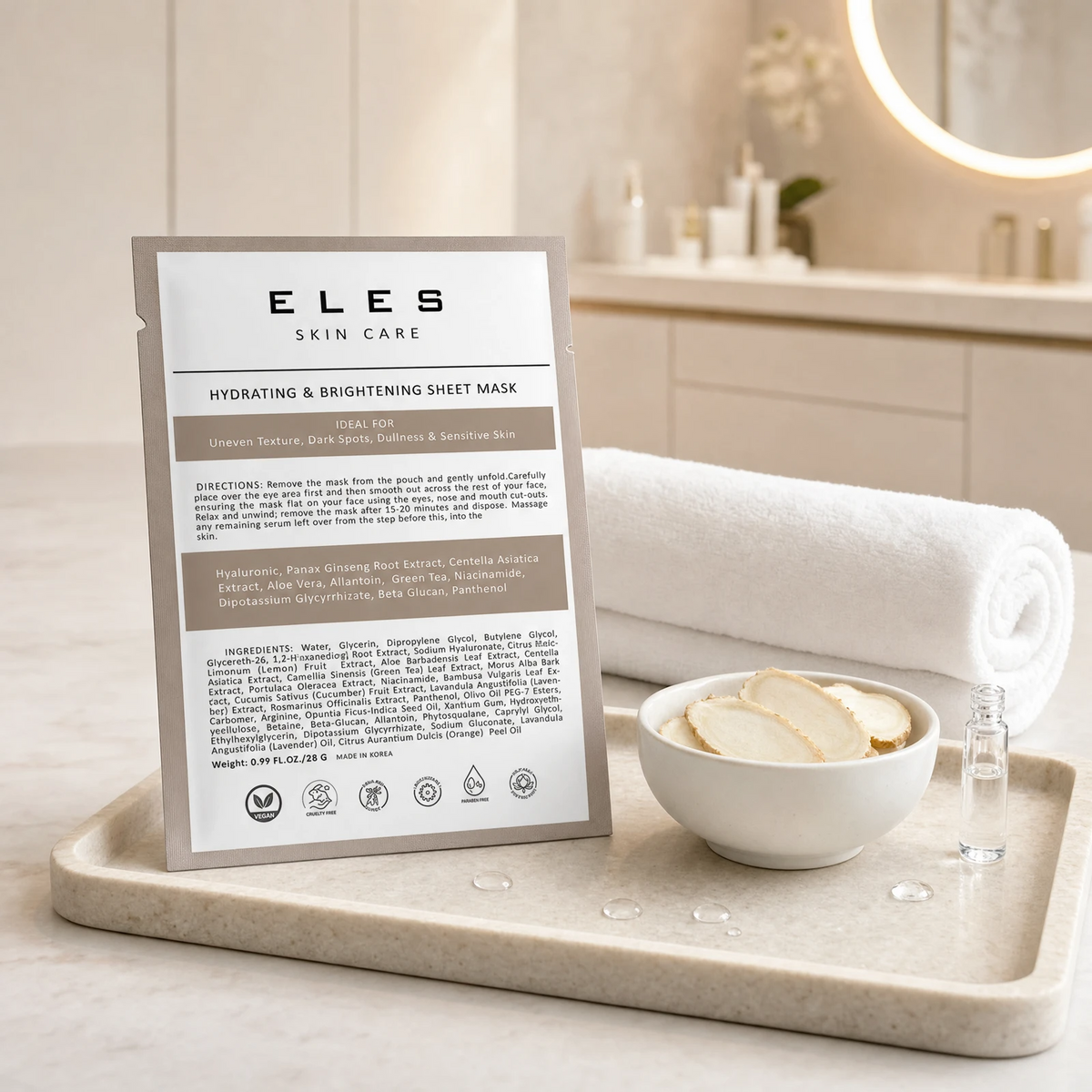 ELES Hydrating and Brightening Sheet Mask warm taupe foil sachet on a stone tray with ginseng root slices and a hyaluronate vial on a marble clinic bench inside a premium skin clinic treatment room