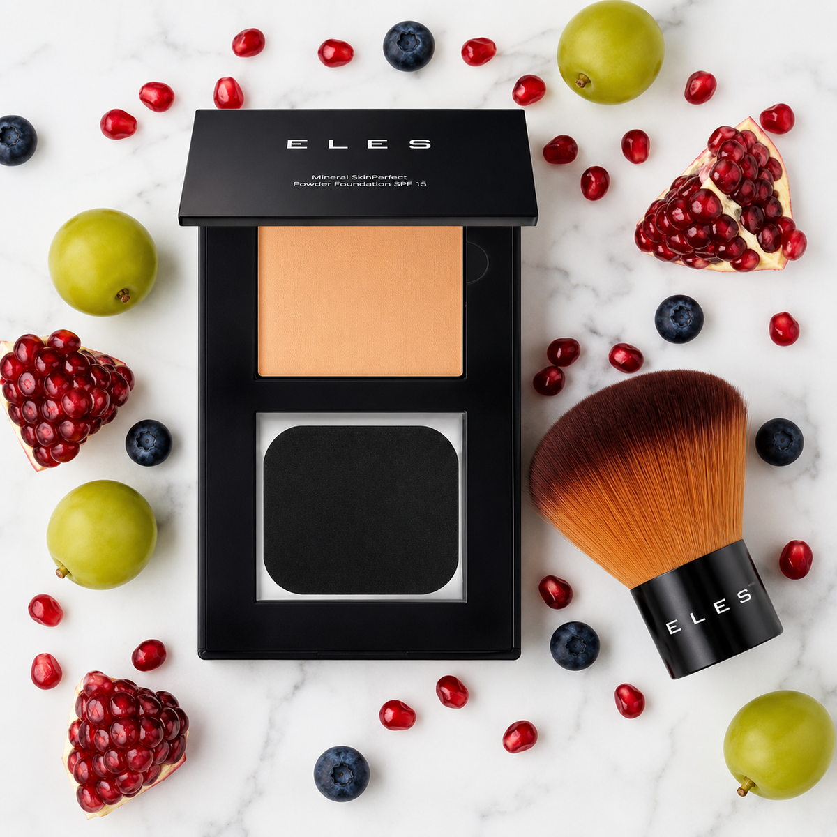 ELES Mineral SkinPerfect Powder Foundation SPF 15 compact open to reveal medium-tan shade, displayed with ELES kabuki brush on marble surface surrounded by fresh pomegranate, blueberries and green grapes.