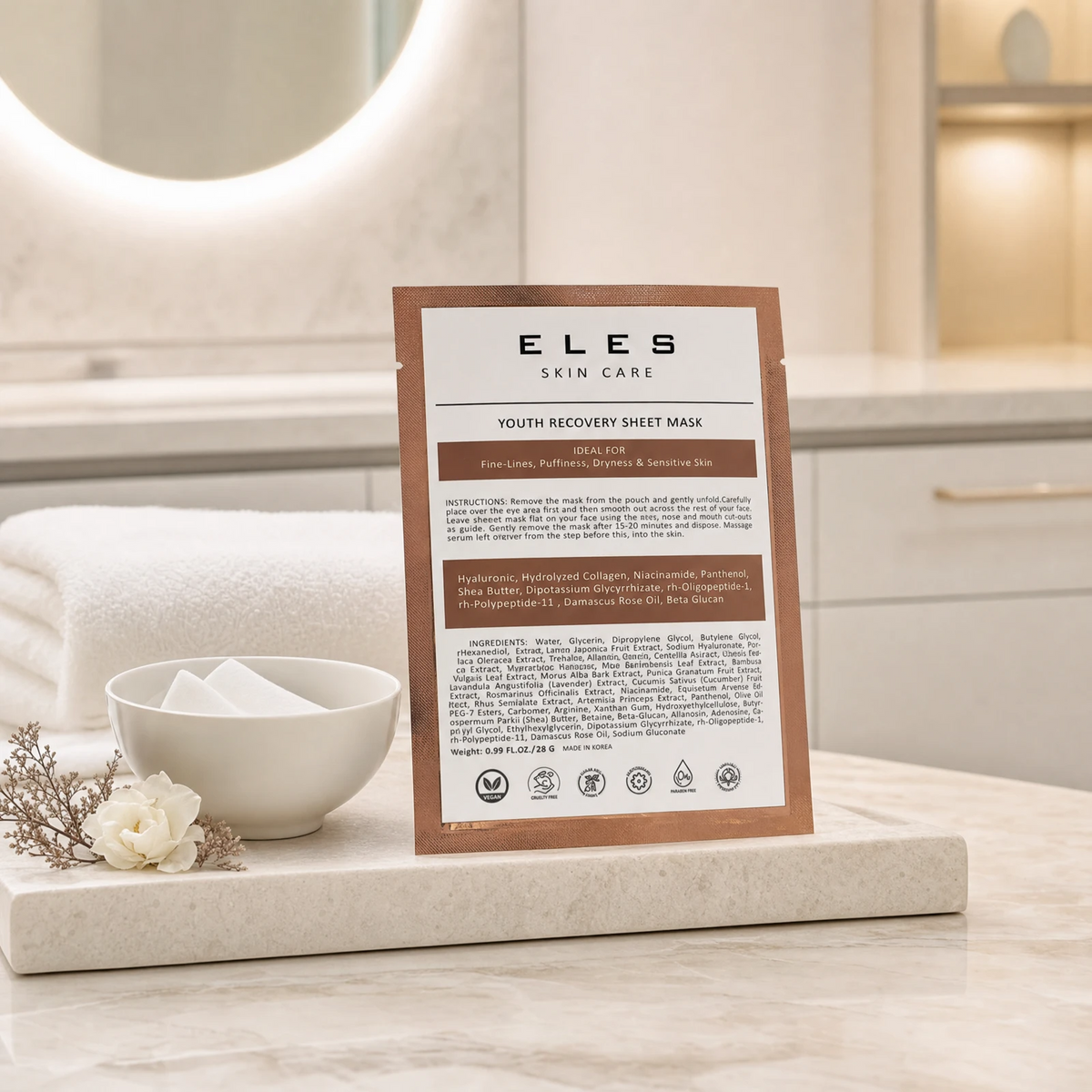 ELES Youth Recovery Sheet Mask bronze foil sachet leaning against a stone tray with a white ceramic bowl and cotton pads on a marble clinic bench inside a premium skin clinic treatment room, ideal for professional facial treatment preparation