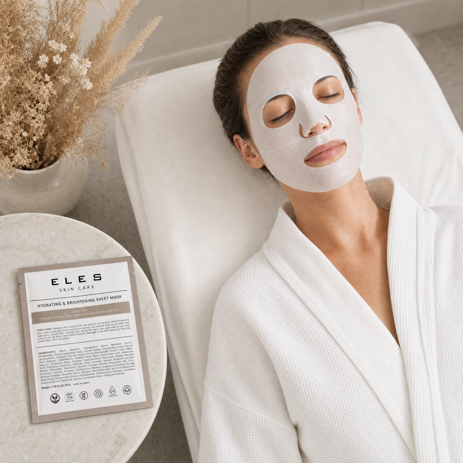 ELES Hydrating and Brightening Sheet Mask applied during a clinical skincare treatment, woman relaxing on treatment bed in white robe, taupe foil sachet on marble side table, uneven texture and dullness treatment