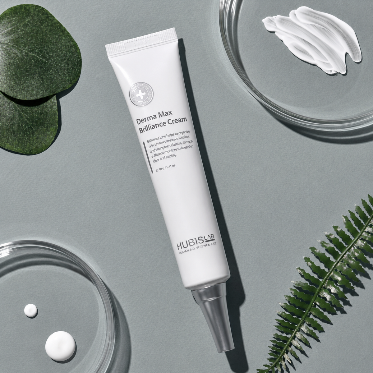 Hubislab Derma Max Brilliance Cream 40ml tube displayed in a grey skincare flatlay with cream texture and botanical accents.