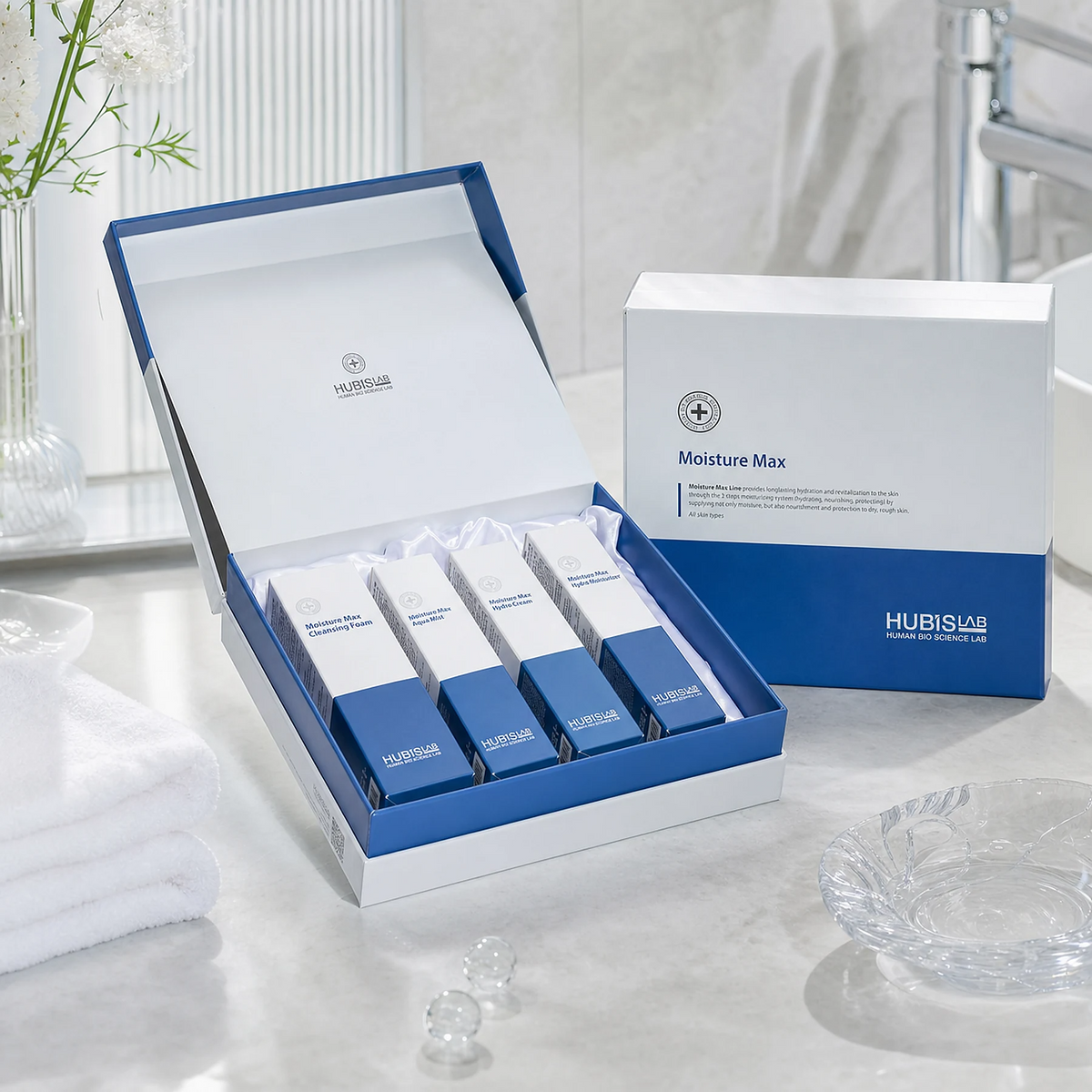 Hubislab Moisture Max Gift Set displayed in a premium bathroom setting with open presentation box, closed gift box, soft towels and clinical-luxury hydration styling.