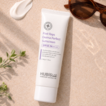 Tube of Hubislab Post Rays Derma Perfect Sunscreen SPF50 PA++++ on a summer skincare flatlay with sunglasses, cream texture and greenery.