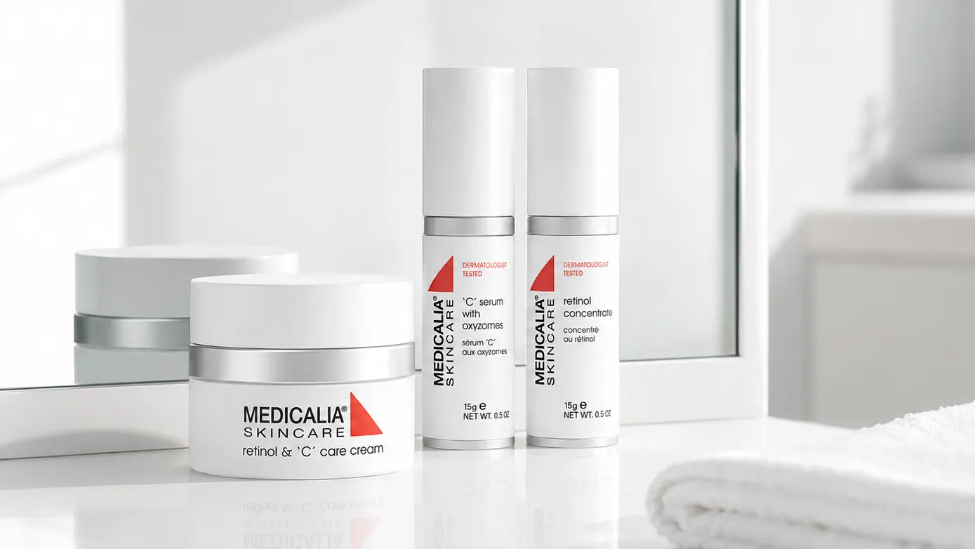 Three MEDICALIA SKINCARE skincare bottles and jars arranged on a glossy white surface in front of a softly blurred bathroom-like background with a mirror and folded towel.