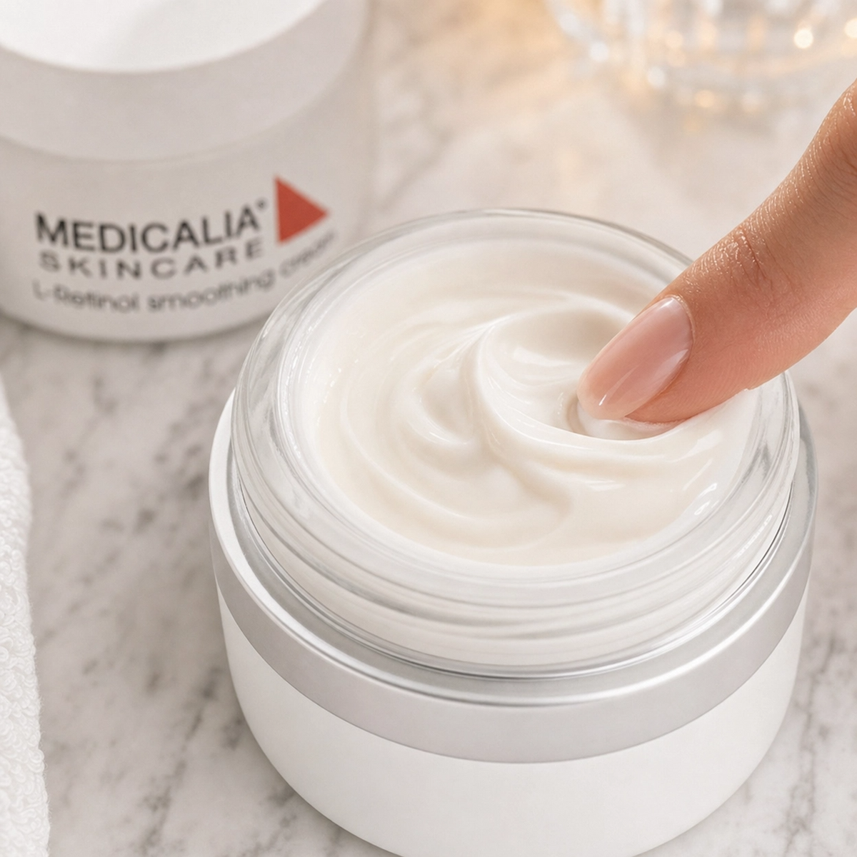Close-up of Medicalia L-Retinol Smoothing Cream being scooped from an open jar showing the rich velvety cream texture with the branded product visible in the background on a marble surface