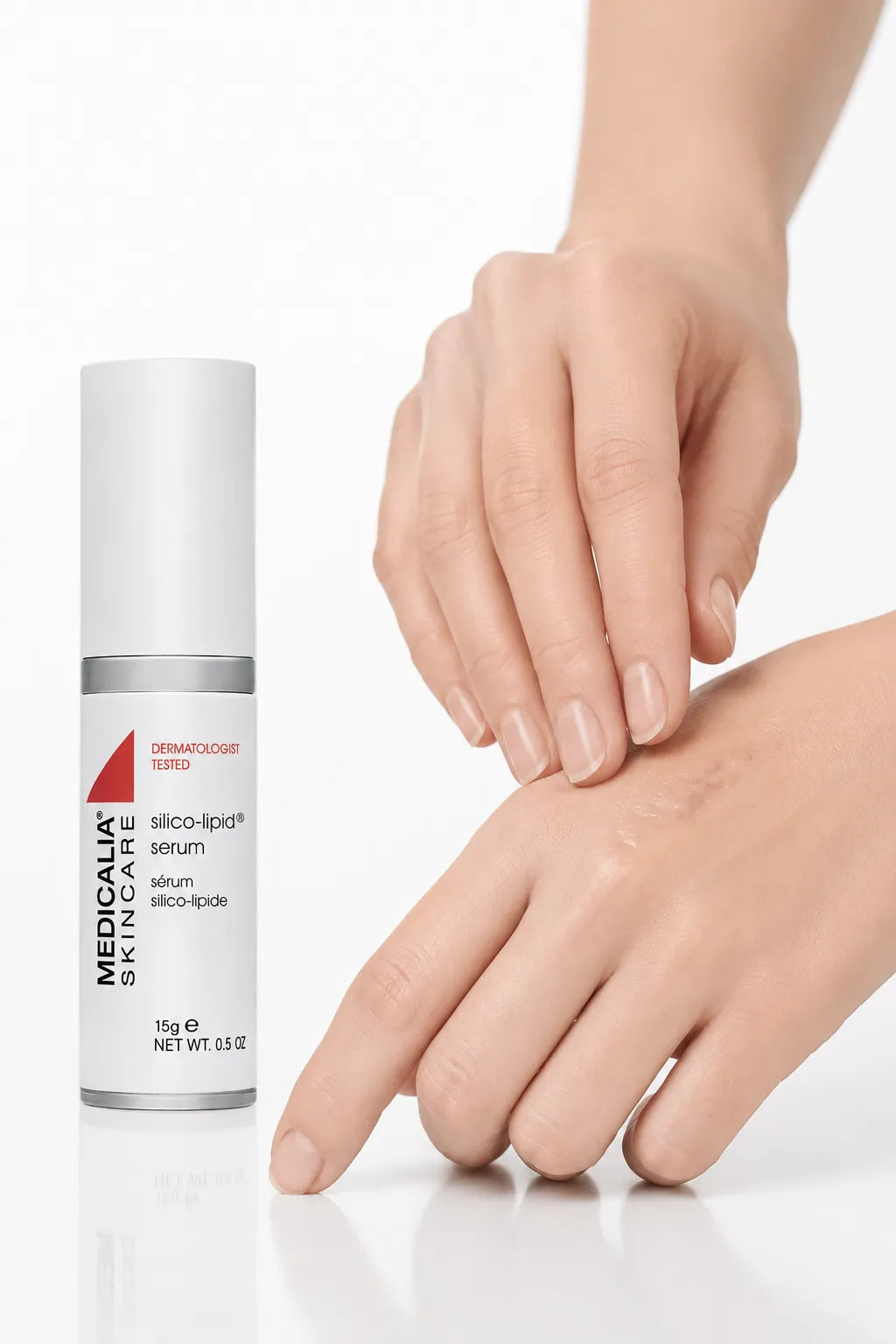 A white cosmetic serum bottle labeled Medicalia Silico-Lipid serum stands beside two hands on a clean white surface, with one hand gently touching the other.