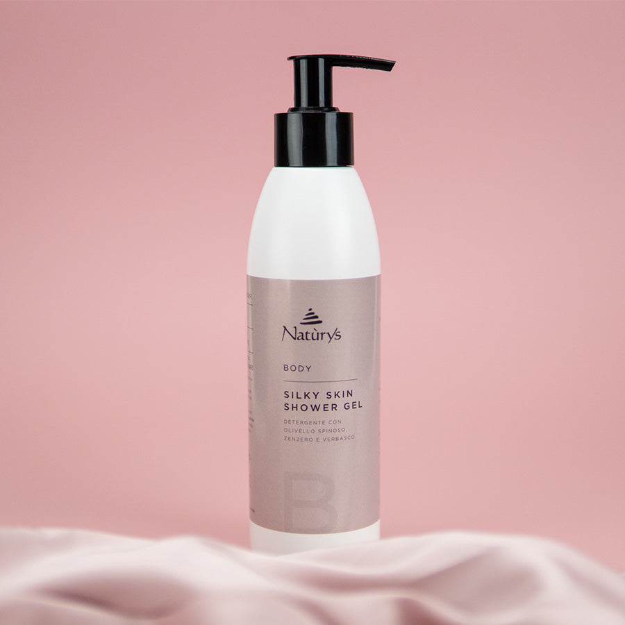 Naturys Body Silky Skin Shower Gel 250ml on a blush-pink marble spa ledge with sea buckthorn berries, fresh ginger root, orange half, and a draped pink silk cloth in a softly steamed luxury spa shower setting
