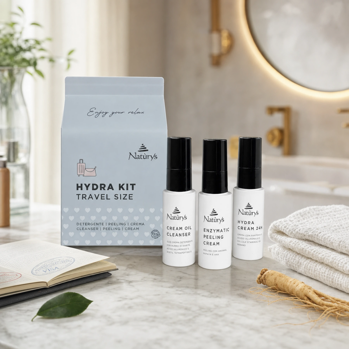Naturys Hydra Kit Travel Set with Cream Oil Cleanser, Enzymatic Peeling Cream and Hydra Cream 24H three 30ml bottles and soft blue-grey travel pouch on a white marble vanity with open passport, camellia leaf, ginseng root and white waffle linen cloth in a luxury hotel spa bathroom setting
