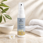 Naturys Sun Cream High Protection SPF30 Spray 100ml white spray bottle on a warm stone vanity with tropical leaf and white flower for Beauty Collective consumer retail.