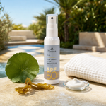 Naturys Sun Cream High Protection SPF 50 Spray 100ml on a travertine pool deck with centella asiatica leaf, golden kelp, sunscreen cream dish and white waffle linen cloth in a luxury outdoor spa setting with blue sky and tropical greenery