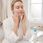 Woman applying Pevonia Sensitive Skin Cleanser 200ml during facial cleansing routine in bright bathroom setting for gentle removal of impurities and comfort for sensitive skin
