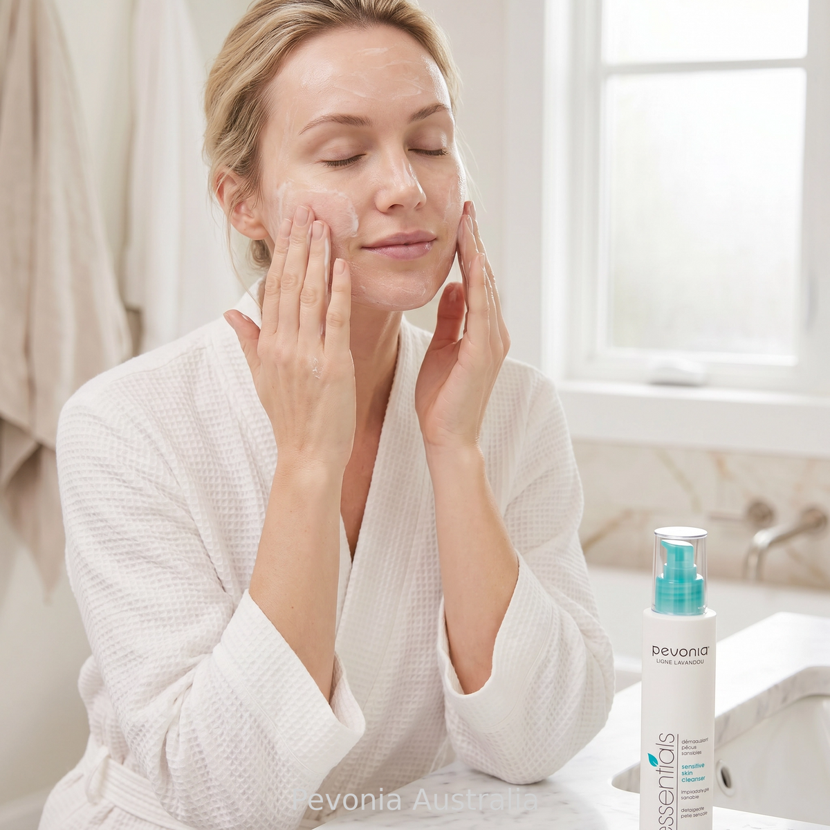 Woman applying Pevonia Sensitive Skin Cleanser 200ml during facial cleansing routine in bright bathroom setting for gentle removal of impurities and comfort for sensitive skin