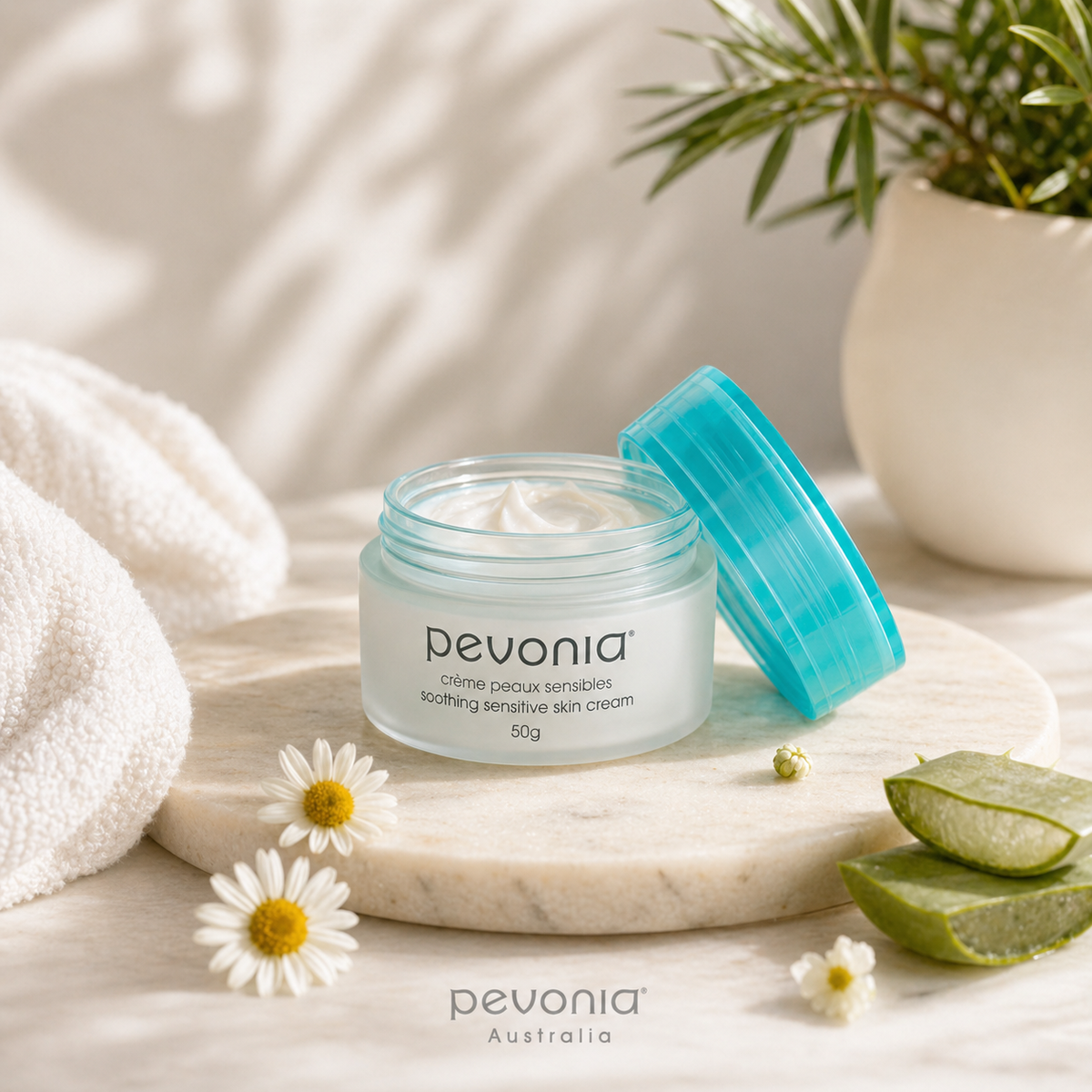 Pevonia Soothing Sensitive Skin Cream 50g open jar lifestyle image with chamomile flowers and aloe vera on marble surface for sensitive skin hydration and calming support