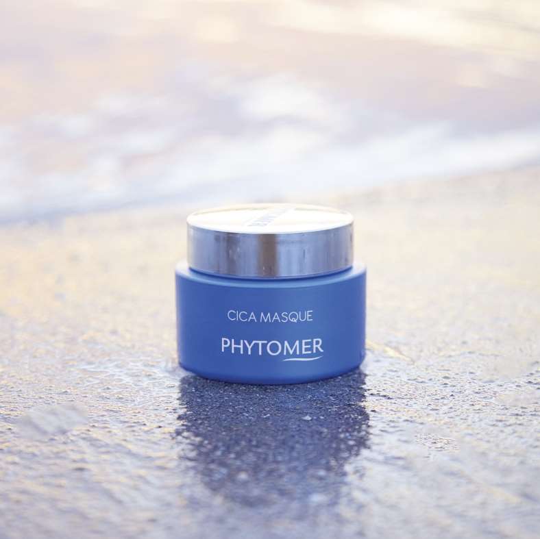 Blue jar of Phytomer Cica Masque - Soothing Ultra-Nourishing Mask 50ml on a reflective surface with a blurred background