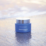 Blue jar of Phytomer Cica Masque - Soothing Ultra-Nourishing Mask 50ml on a reflective surface with a blurred background