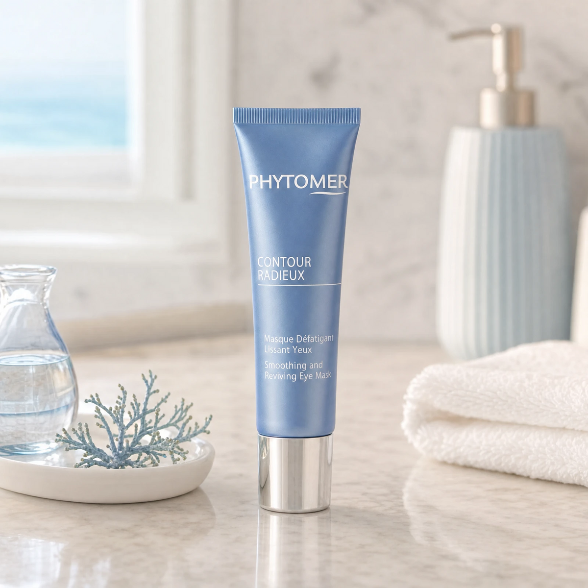 Phytomer Contour Radieux Smoothing and Reviving Eye Mask 30ml on a marble bathroom counter with teal coral in ceramic dish, glass vase with water, gold pump dispenser and white towels, premium at-home skincare setting