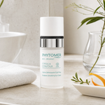 Phytomer Cyfolia Organic Radiance Smoothing Eye Cream 15ml on a marble bathroom counter with orange peel in ceramic dish, botanical in glass vase, rosemary sprig and white towels, premium at-home organic skincare setting