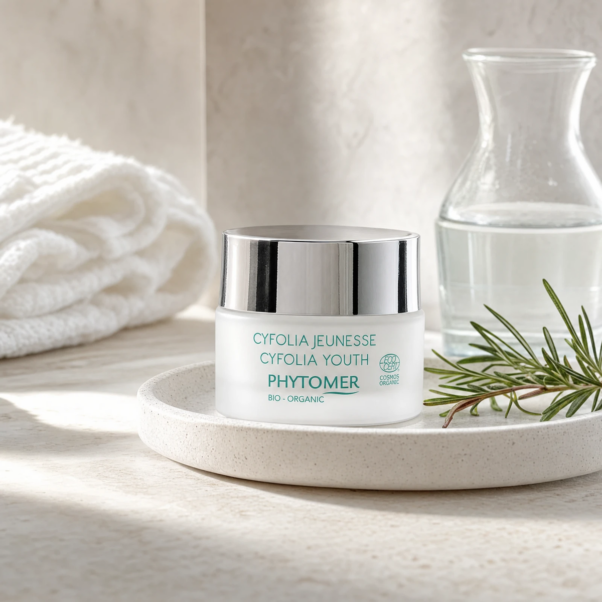 Phytomer Cyfolia Organic Youth Glow Renewing Wrinkle Cream 50ml on a stone bathroom vanity tray with rosemary, glass vessel and white towels, premium at-home organic skincare setting