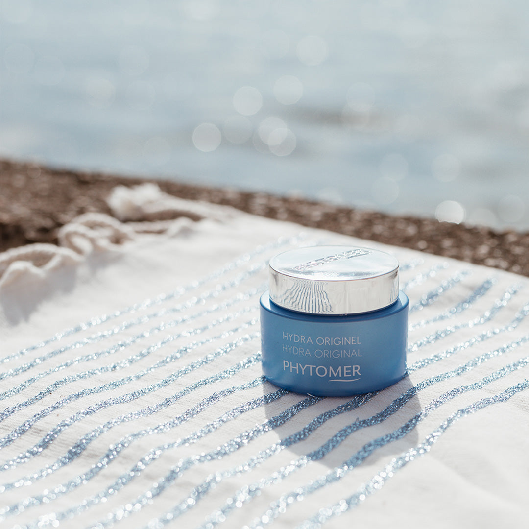 Phytomer Hydra Original Moisturising Melting Cream displayed on a beach towel by the sea, showcasing deep hydration and comfort for dry and dehydrated skin.
