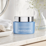Phytomer Nutritionnelle Dry Skin Rescue Cream 50ml on a marble bathroom counter with gypsophila in glass carafe, sea sponge in ceramic dish, white waffle towel and round mirror, premium at-home skincare setting