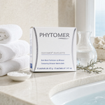 Phytomer Oligomer Silhouette Contouring Enhancer Marine Bath 8 sachets on a marble bath surround with mineral crystals in ceramic dish, glasswort sprig, glass carafe, white coral and white spa towels, premium at-home spa bath setting