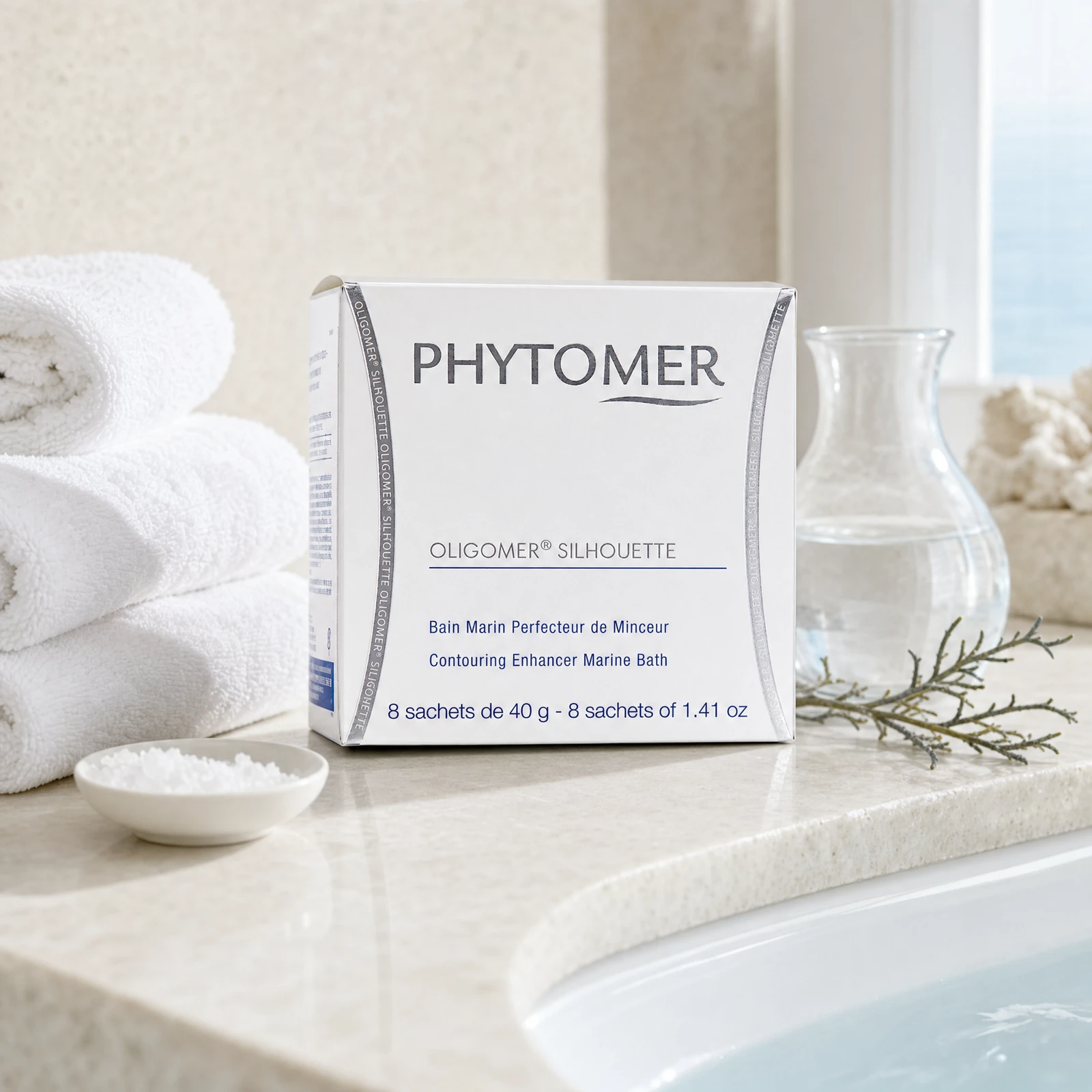 Phytomer Oligomer Silhouette Contouring Enhancer Marine Bath 8 sachets on a marble bath surround with mineral crystals in ceramic dish, glasswort sprig, glass carafe, white coral and white spa towels, premium at-home spa bath setting