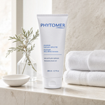 Phytomer Oligomer Well-Being Sensation Moisturising Shower Gel 200ml on a marble shower shelf with white towels, glass vessel and coastal botanical, premium at-home bathroom setting