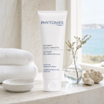 Phytomer Oligomer Well-Being Sensation Strengthening Moisturising Body Cream 150ml on a marble bath surround with gypsophila in glass carafe, white coral, ceramic dish, white spa towels and sea view, premium at-home body care setting