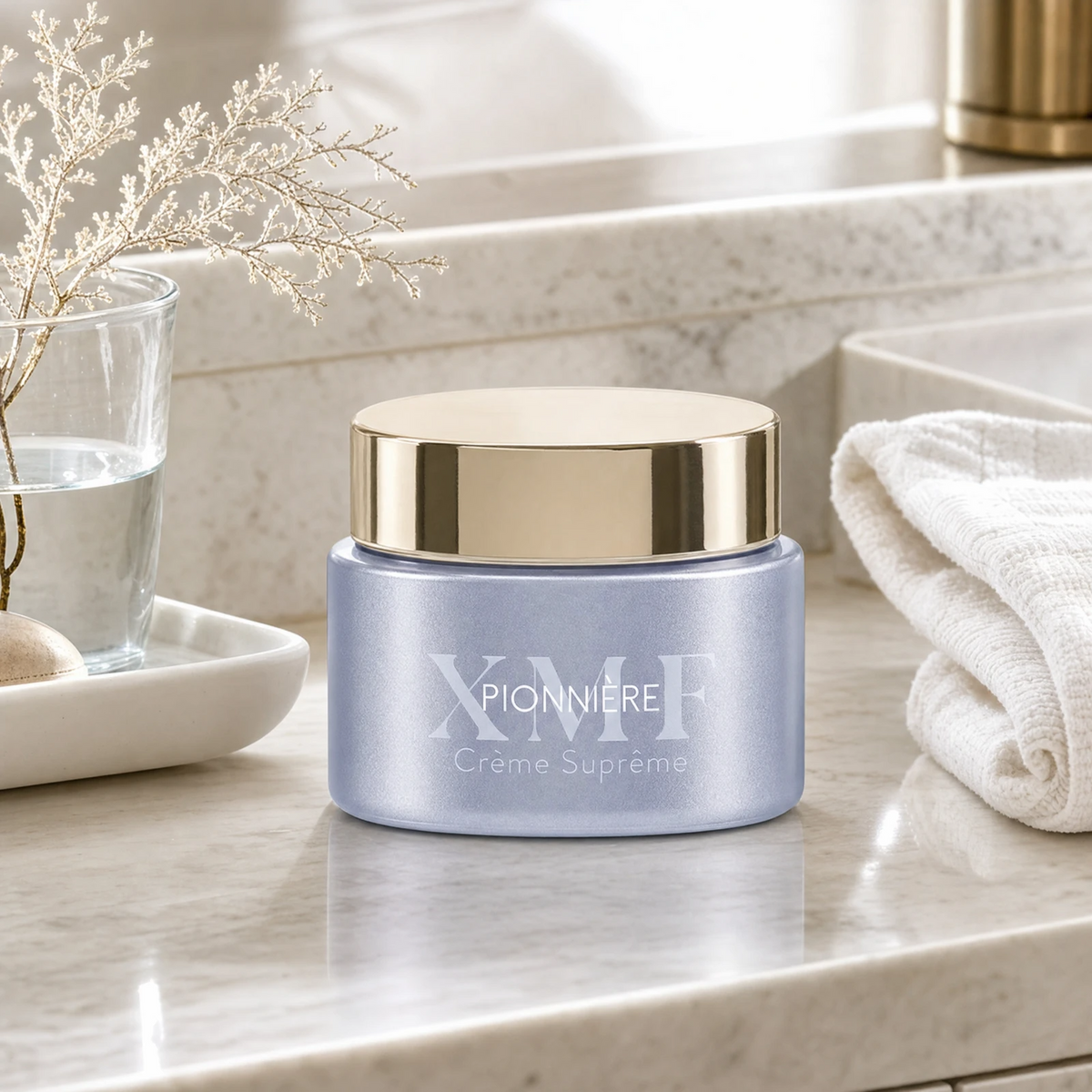 Phytomer Pionniere XMF Youth and Glow Supreme Cream 50 ml on a marble bathroom counter with gypsophila in glass carafe, white ceramic tray with sea pebble, white waffle towel and gold bathroom accessory, premium at-home skincare setting