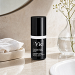 Vie Collection Chrono Eyes Puffiness Dark Circles Wrinkle Cream 15ml on a marble bathroom counter with gypsophila in glass carafe, white waffle towel in stone tray, white basin and round mirror, premium at-home skincare setting