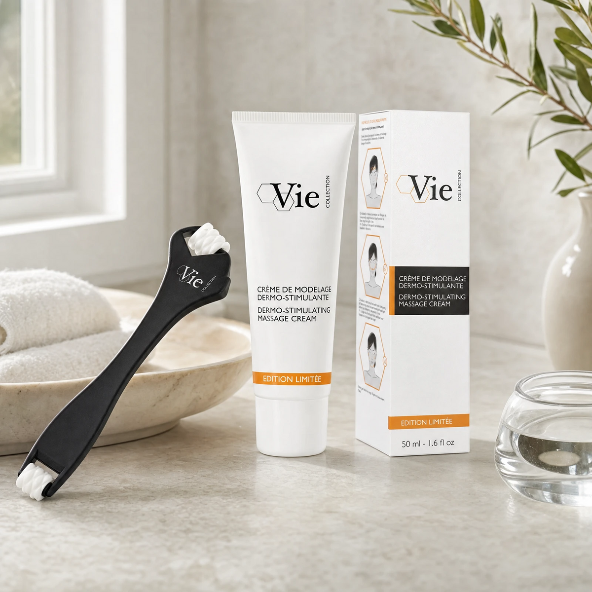 Vie Collection Dermo-Stimulating Massage Cream 50ml Limited Edition with facial roller applicator and retail box on a marble counter with olive branch in white vase, marble bowl with towels and soft window light, premium at-home skincare setting
